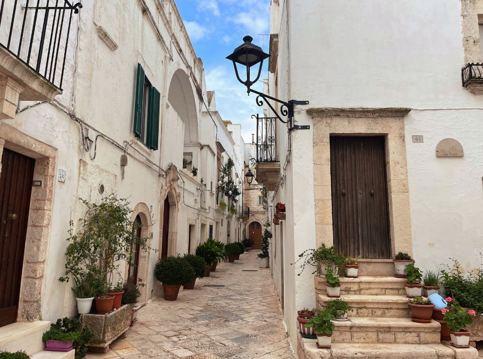 narrow streets with white building decorated with pots of plants and flowers in locorotondo puglia