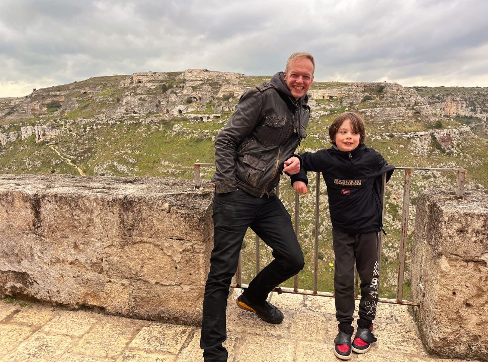 father and son posing in front of a view of the mountain accross Matera city with ancient caves