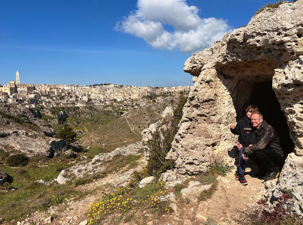 father and son sitting at a cave entrance with in the back full view of Matera city Italy