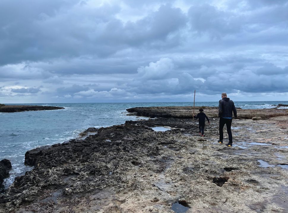 father and son walking on the rocky shore on a cloudy day in Torre Santa Sabina Puglia 