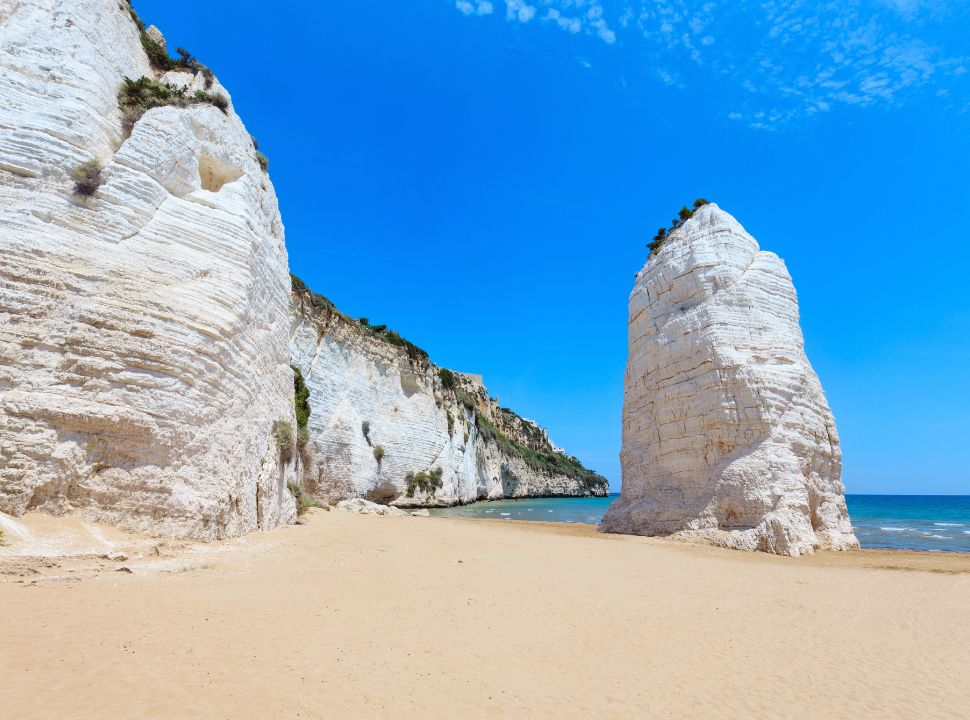 limestone cliffs and tall pillar at a sanded beach with beautiful blue water in gargano area Puglia