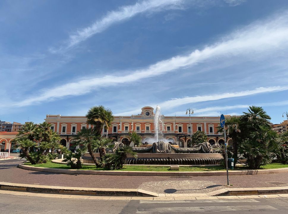 front view of the colourful bari train station building with a fountain in front