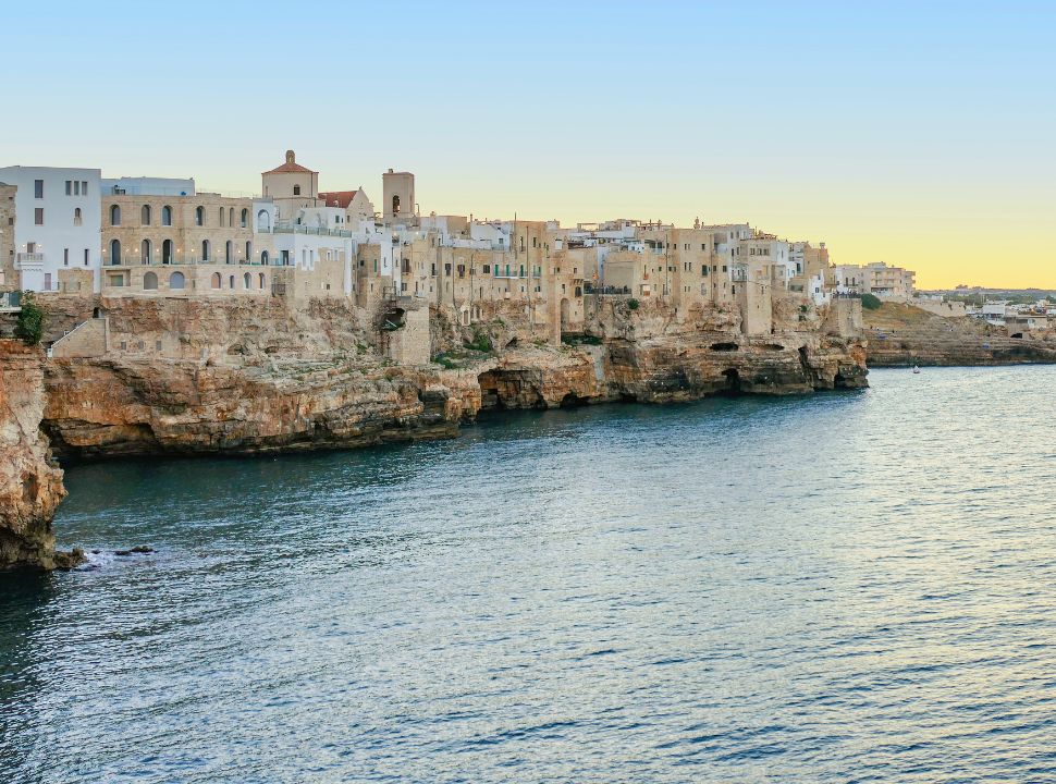 view of the cliff buildings in polignano a mare with the sun set in the back