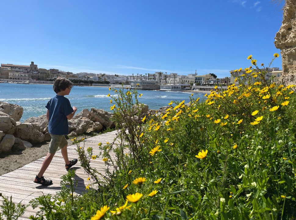 boy walking along a wooden walkway along the cliffs at otranto beach puglia