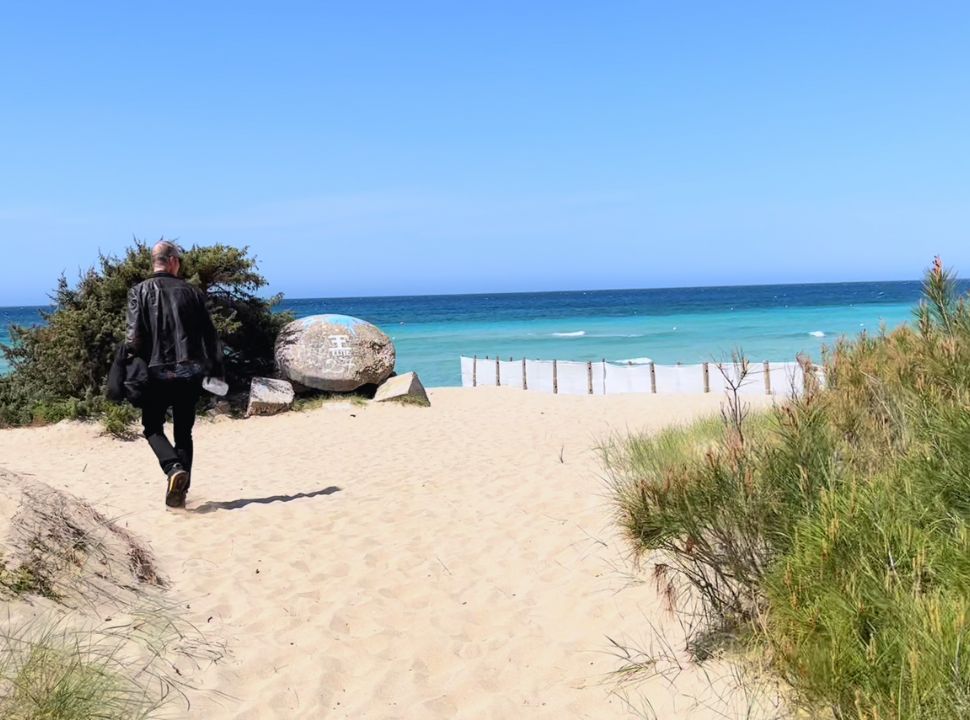 man heading to the soft sanded beach with in the back ground light blue water in Puglia Italy