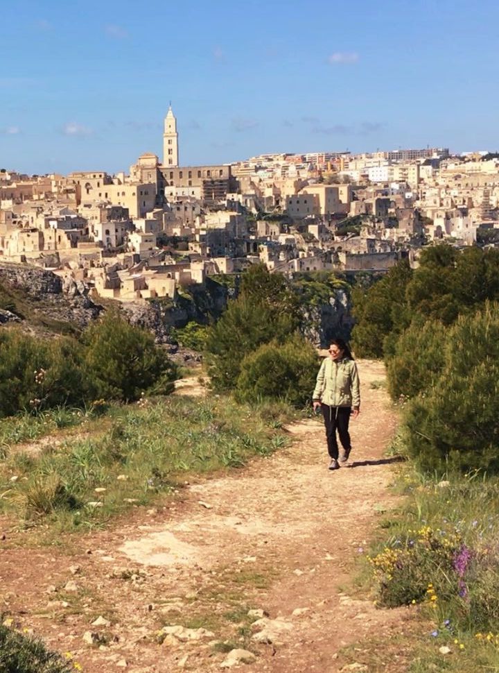 woman walking along a nature trail with view of the ancient town matera in the back