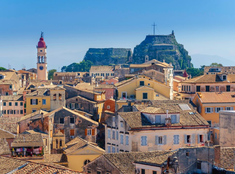 view of the old colorful houses of corfu town, with a tall church bell tower and the old fortress dominating the view