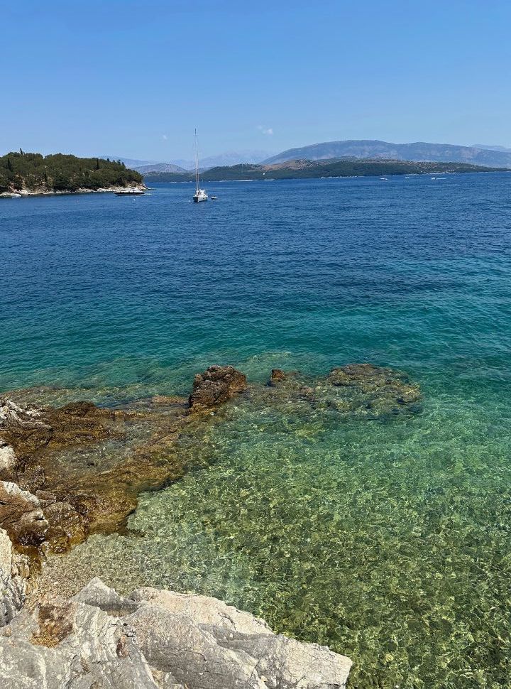 crystal clear water and a sailboat anchored just off the coast at Agios Stefanos East Corfu