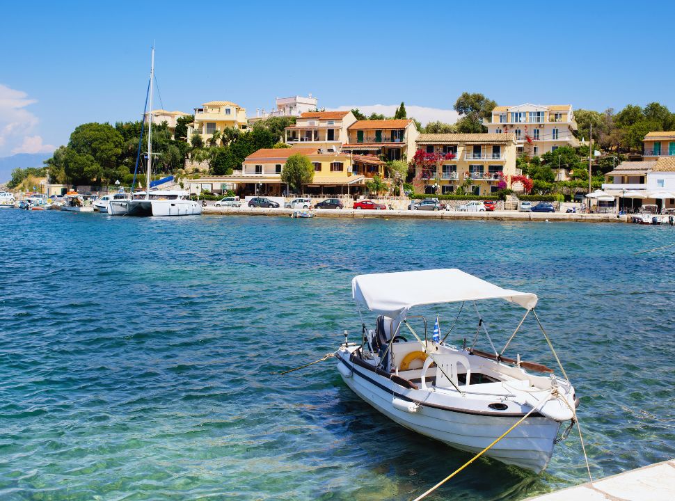 small boat docked at a harbour with in the far back houses along the water in kassiopi, a village in north east corfu