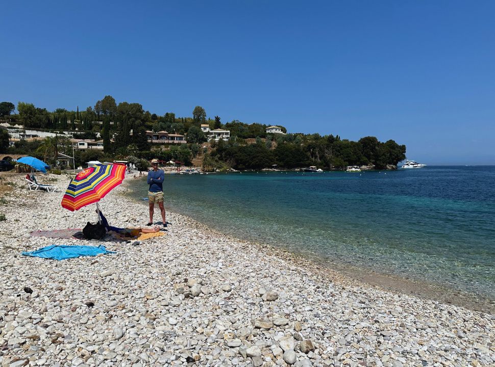 man standing at a quiet pebbled beach with crystal clear water in east Corfu Island