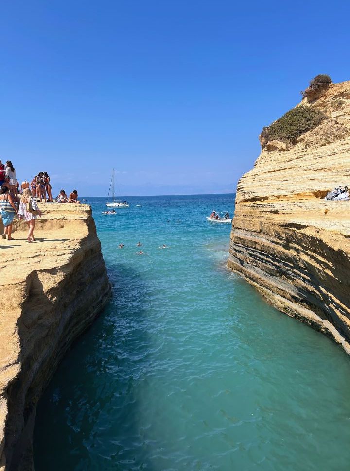 view between the cliffs at canal d'amour where people are swimming the in the water and sitting on the cliffs edge. 