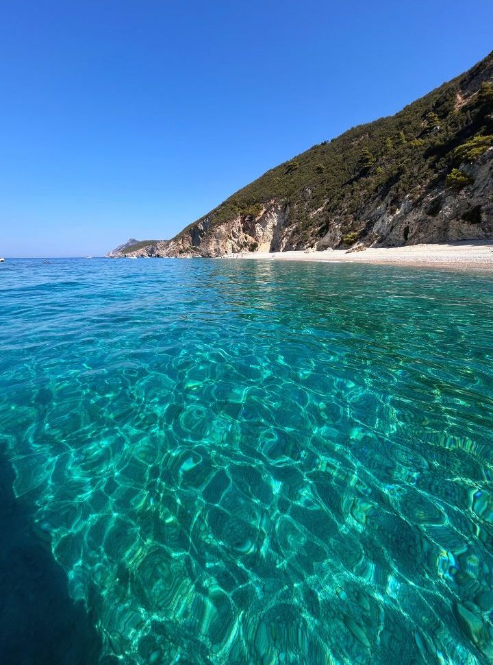 Turquiouse water and a small white pebbled beach seen from the boat at corfu island