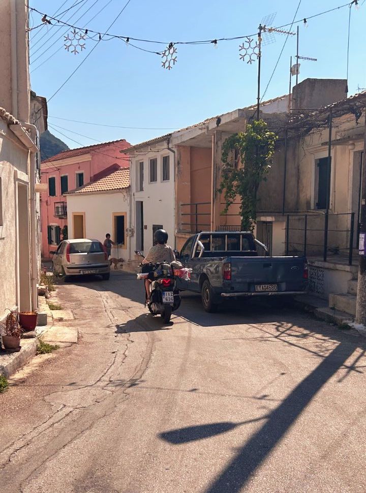 woman driving a scooter through a little mountain village in corfu island