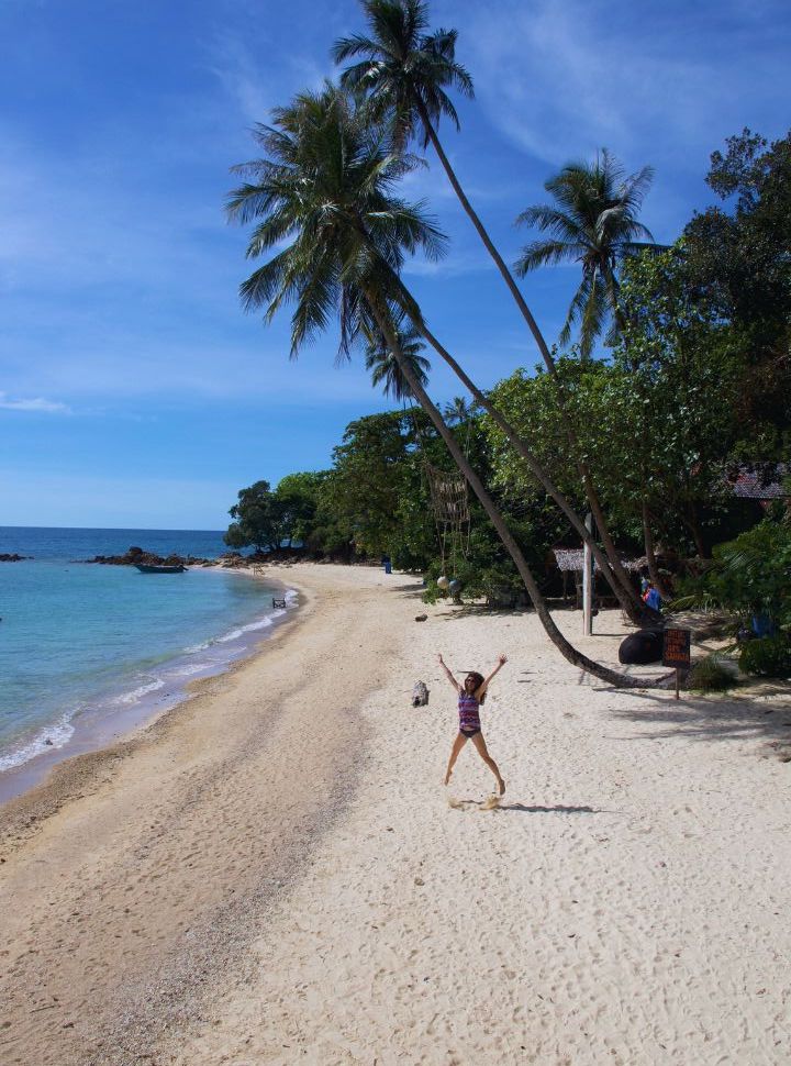 woman jumping in the air on a tropical beach with white sand and blue ocean on kapas island malaysia