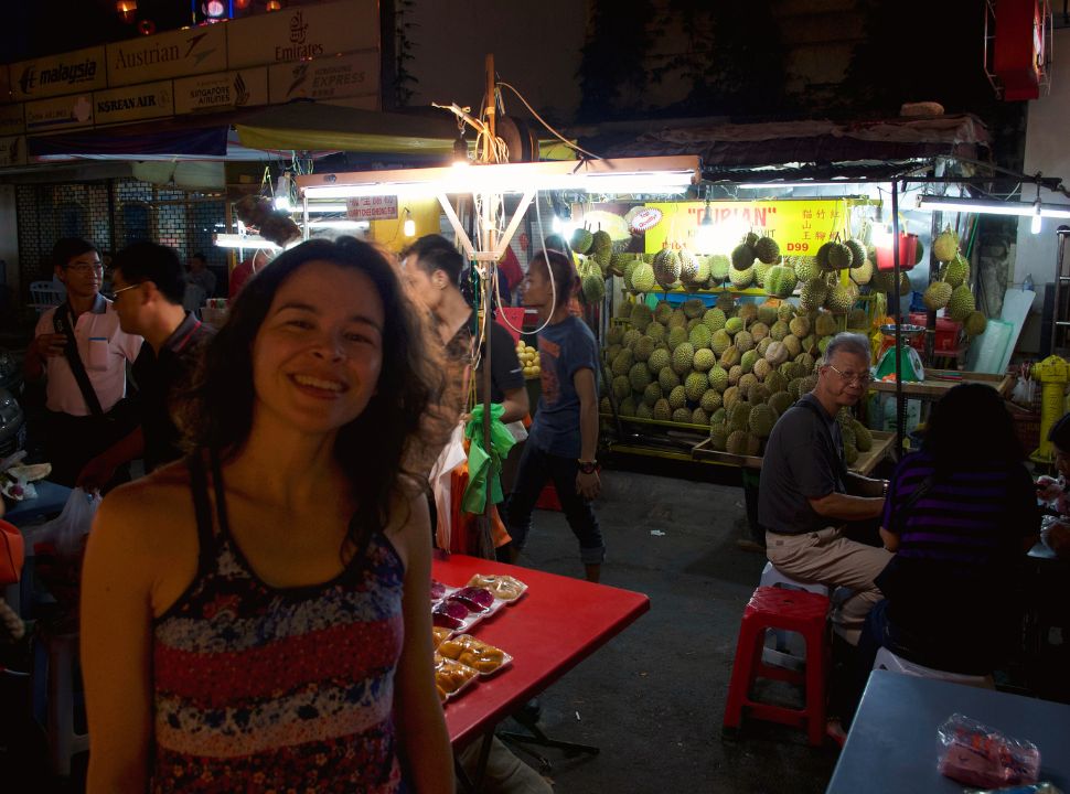 woman posing in front of a fruit stand that sells durian in kuala lumpur malaysia