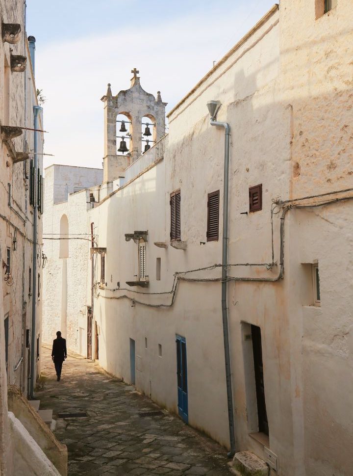 man walking through a narrow cobbled streets with white buildings in ostuni Puglia