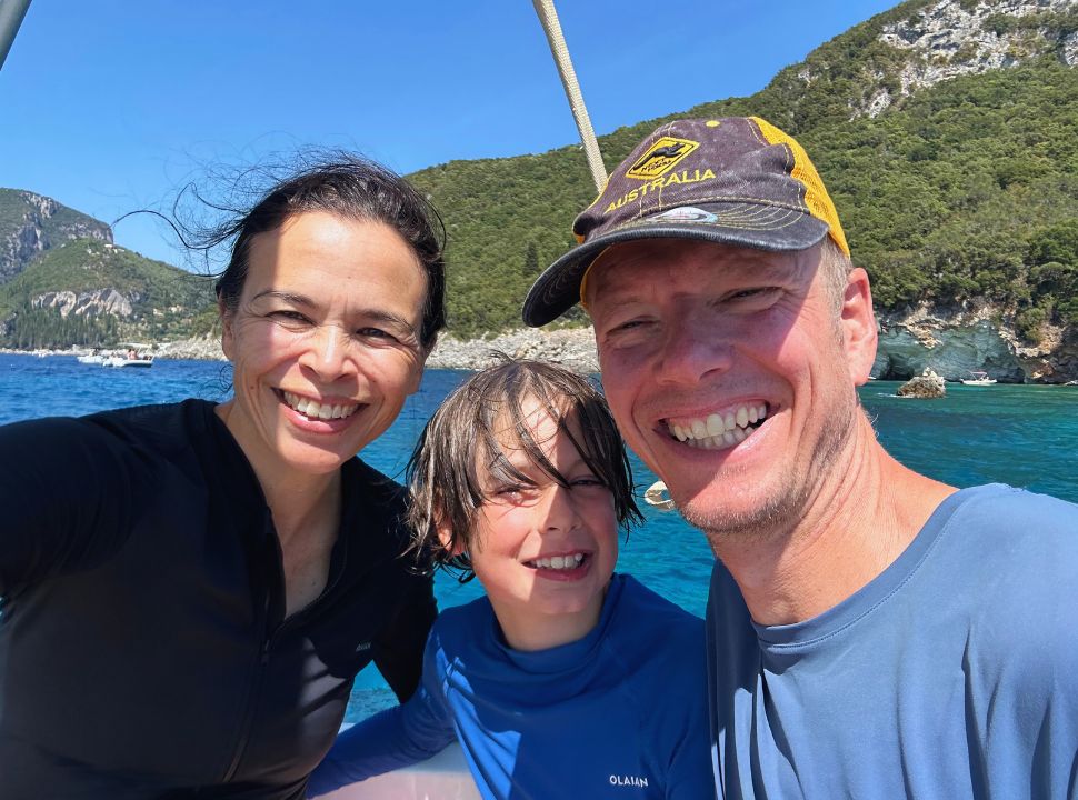 family posing on a boat with beautiful emerald blue water and greens hills in the back