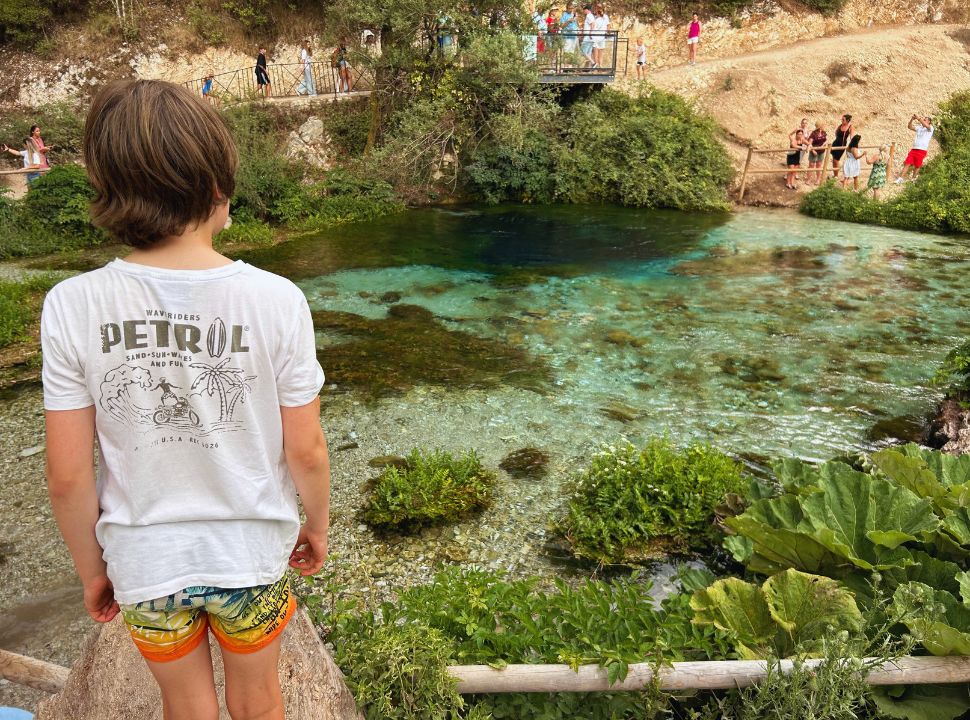 boy looking over the blue eye, on the other side of the water is a balcony where visitors can view the natural spring from above