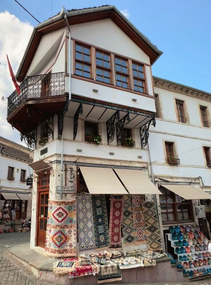 while tall ottoman house with a souvenir shop displaying carpets and colored plates in Gjirokastër Albania