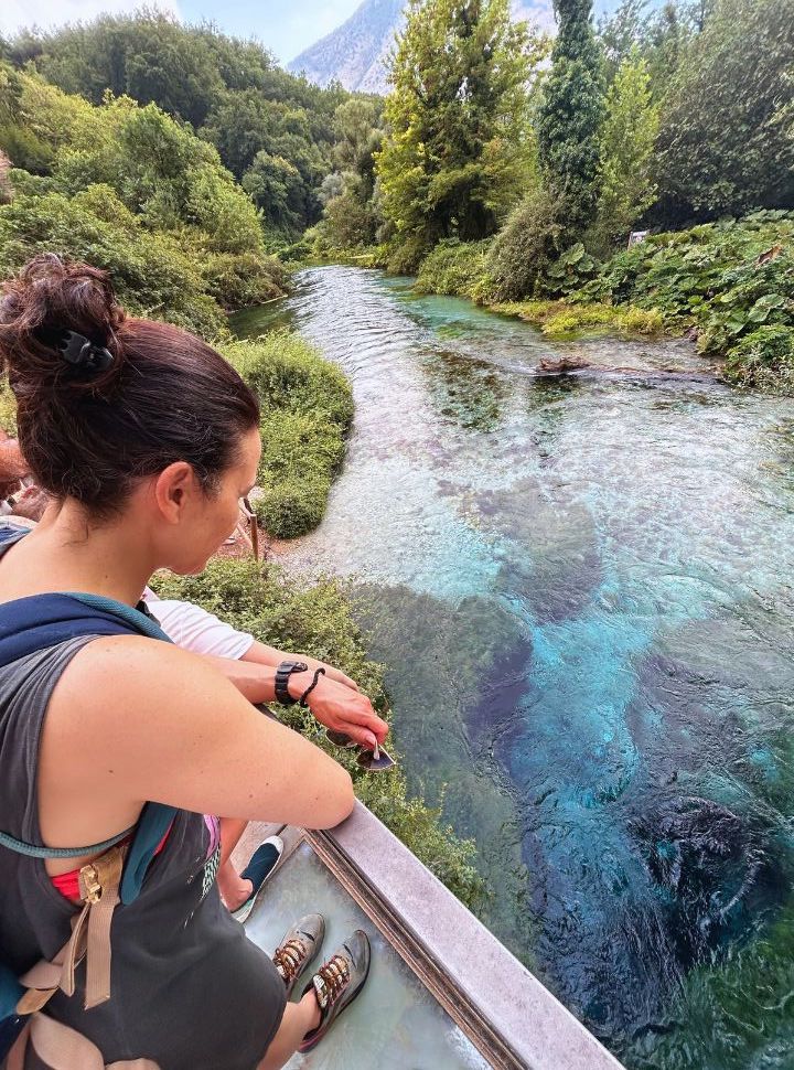 woman standing on a plateau looking down at the blue eye natural spring, the river flows through lush vegetation at the blue eye in albania