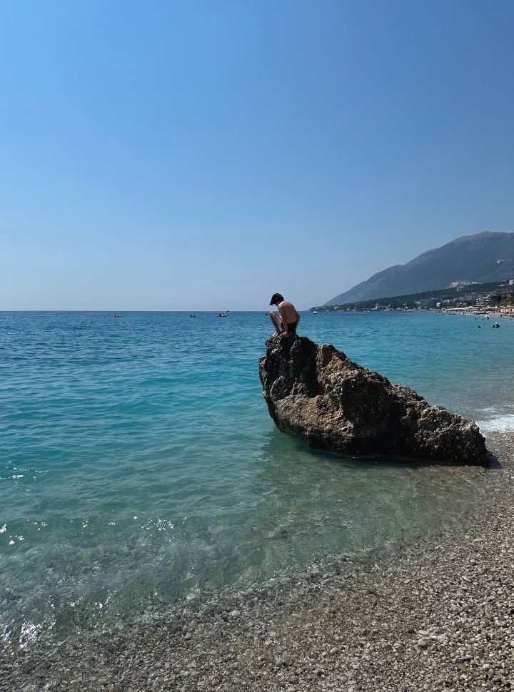 boy on top of a large rock looking down into the water and ready to jump in at Dhermi Beach