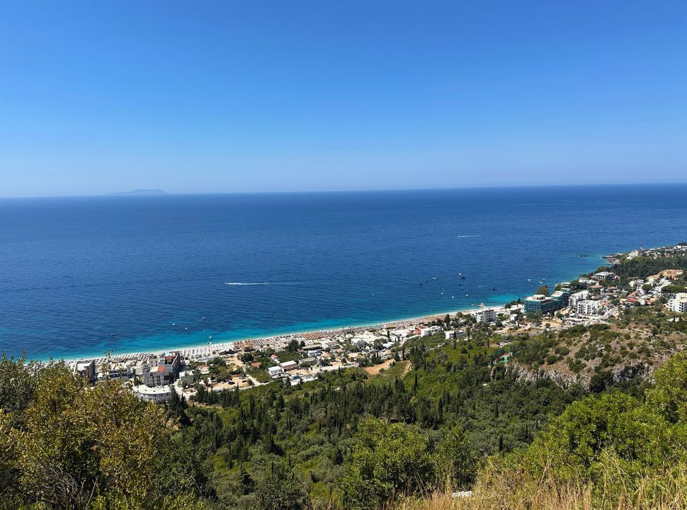 view of Dhermi beach fully built with accommodation, beaches are full of sun beds, the ocean water is dark blue and turquoise