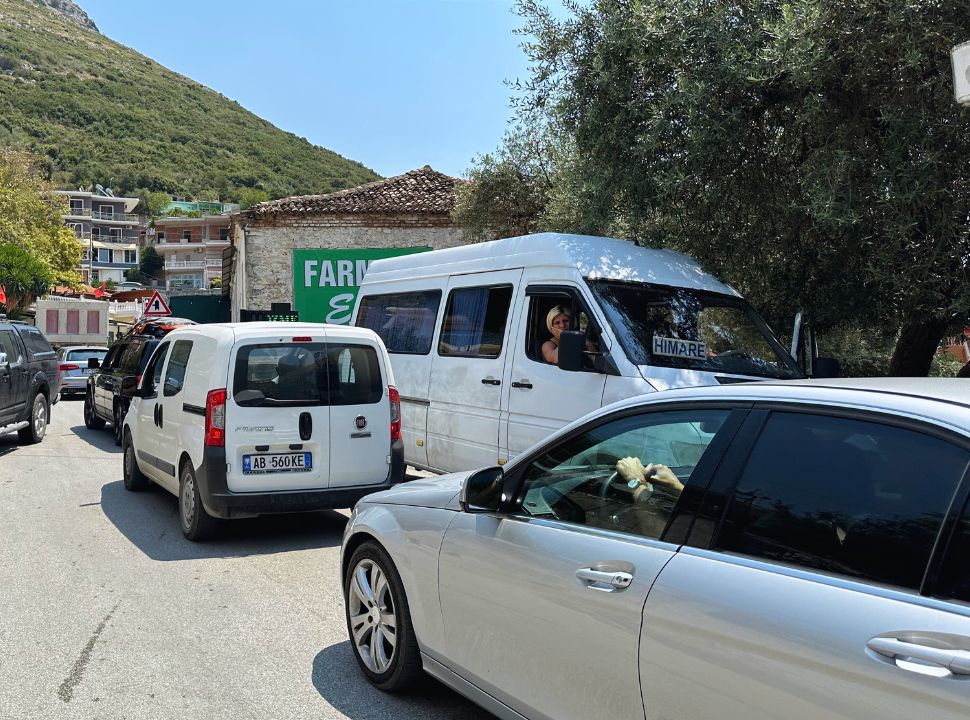 traffic at the main street of Dhermi Town, a small mini bus with the sign Himare is parked near the olive trees