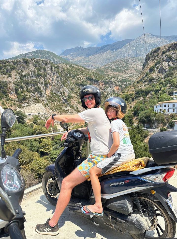 father and son at on a motorscooter enjoying mountain and village view of Dhermi Albania