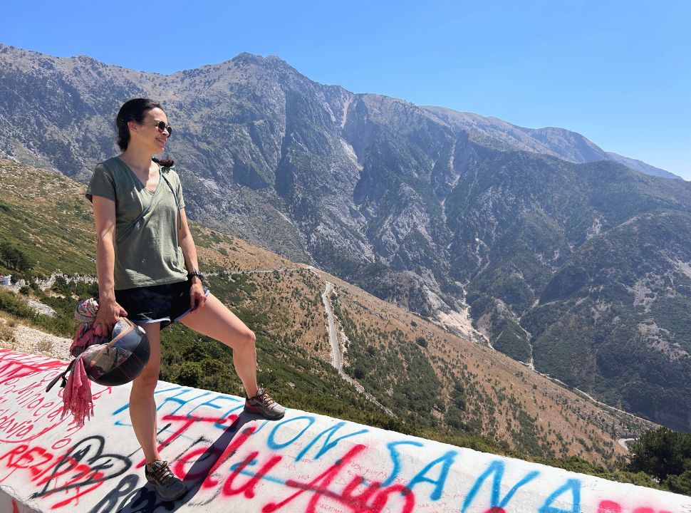 woman admiring the view of the Albanian coastline with stunning mountains in the back, you can see a road going down 