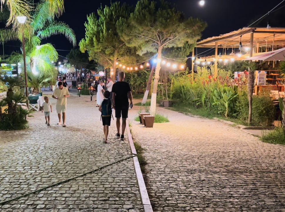 father and son walking along a beautifully lit beach club, which trees and plants at Dhermi beach Albania