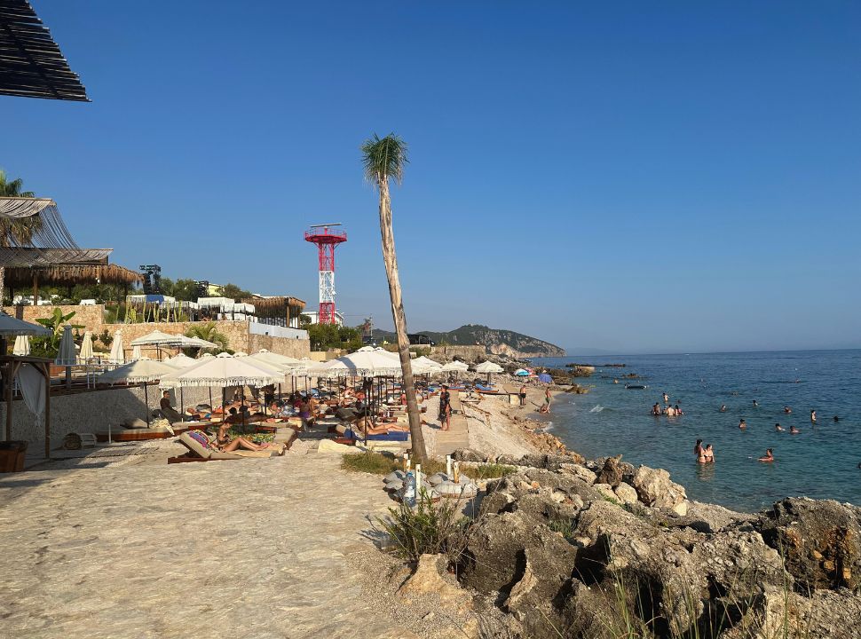 beach club with a row of white sun umbrellas and beds, people enjoying a swim in the water at Palasa Beach Albania