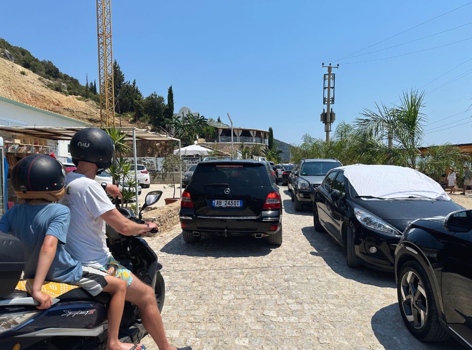 father and son on motor scooter standing in a traffic jam of cars finding a parking spot at Dhermi beach Albania