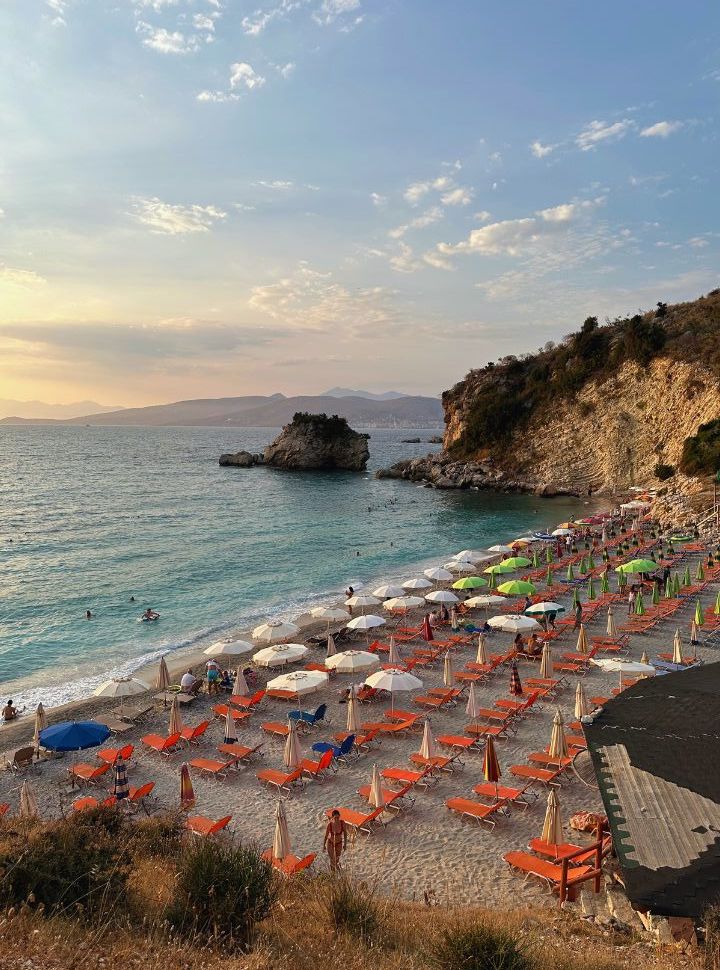 view from the cliffs of a small coved beach covered with orange sun beds, just before sunset. The beach is empty at plazhi i pasqirave ksamil