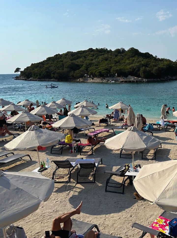 white sun umbrellas with sun beds on a small patch of white sand with in the distance a small island in Albania