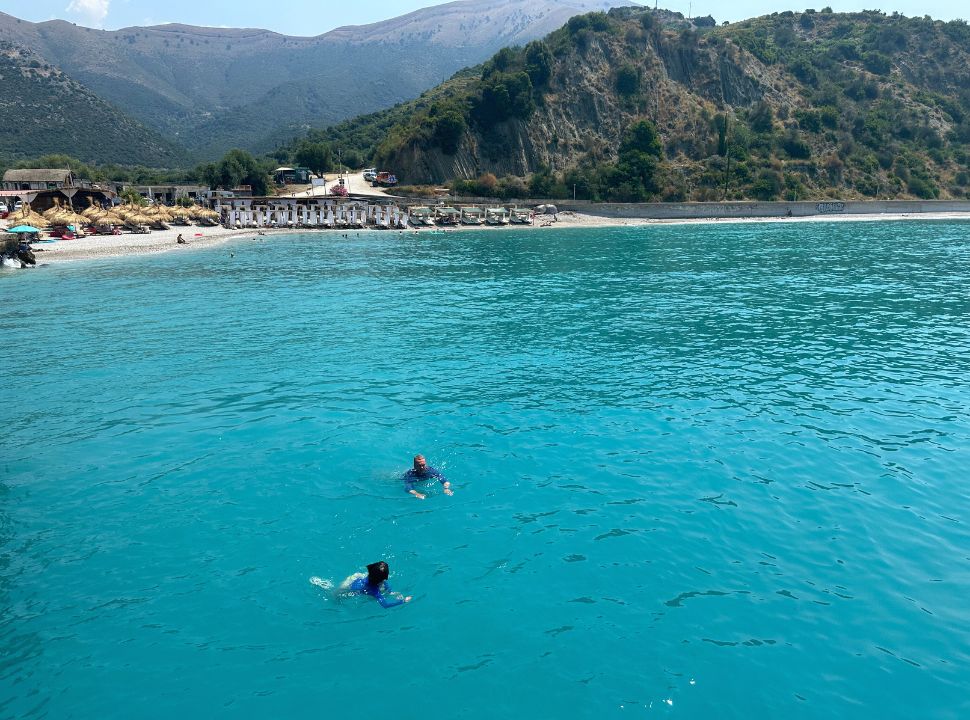 father and son swimming in bright blue water just off the coast at buneci beach in albania