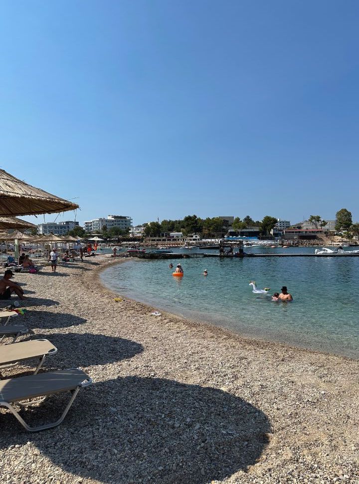 quiet pebbled beach with sun loungers and a couple of people swimming in the clear water