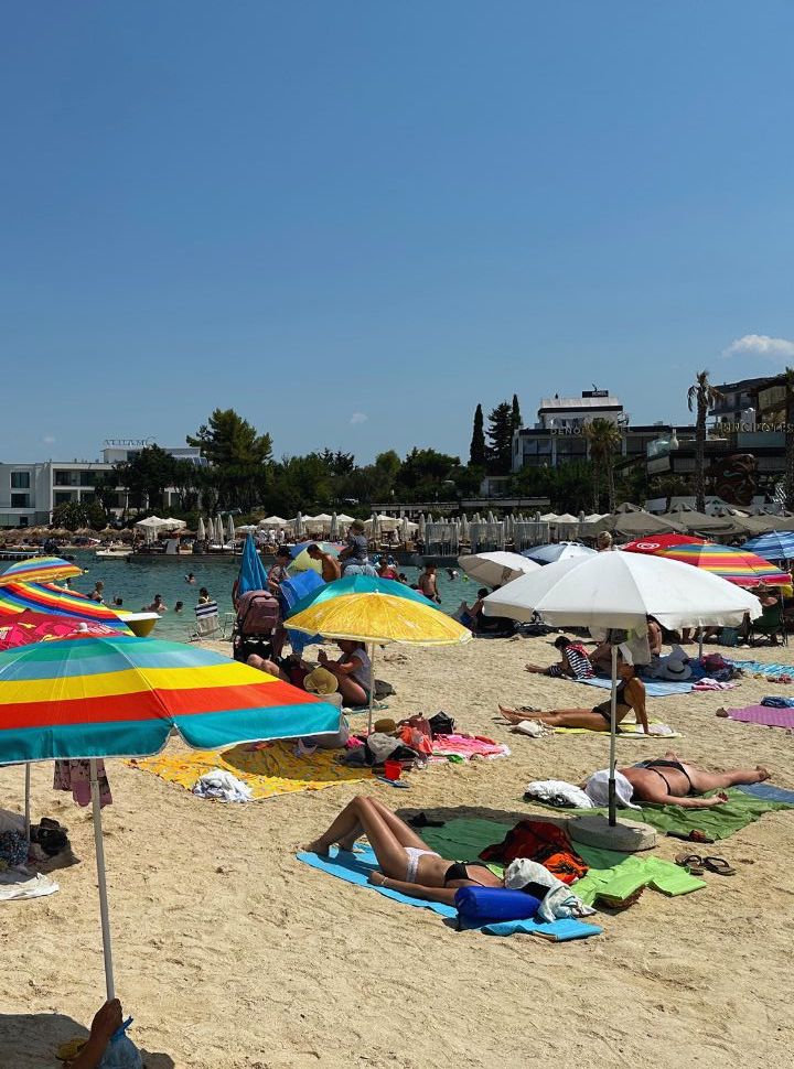 different colored sun umbrellas at a small strip of beach where people are lying in the shade and sunbathing