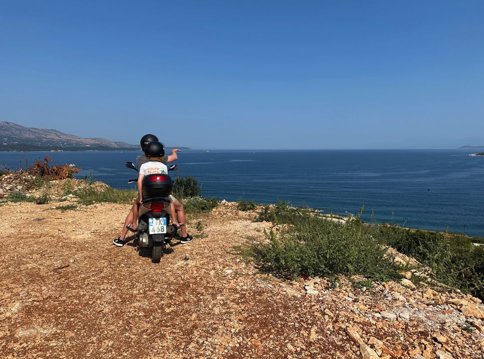 father and son on a motorscooter enjoying the view over the ocean just before ksamil albania