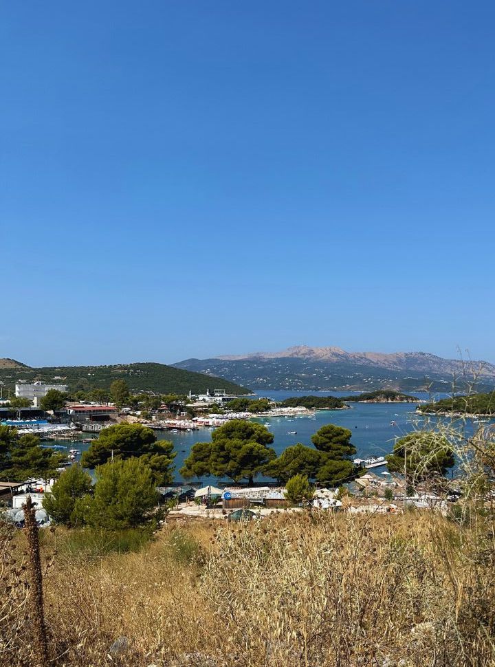 view of ksamil bays with buildings, beach clubs and boats at waterfront. Mountain range in the far back