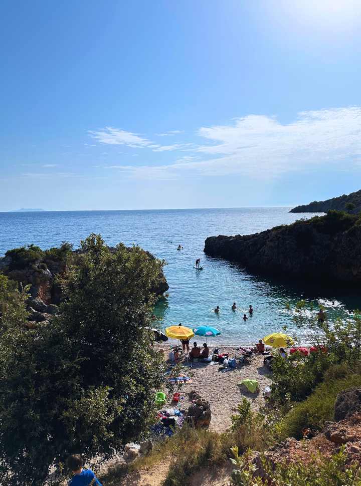 view of a small beach set within rocky cliffs with people enjoying the beach in Albania