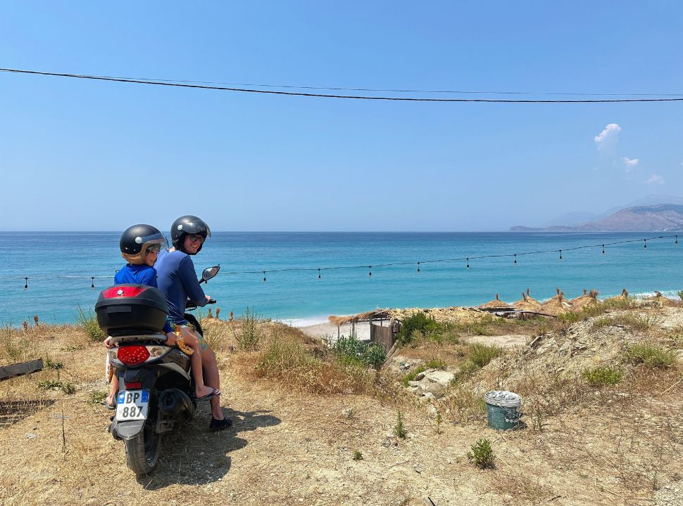 father and son on a motorscooter looking over a quiet beach and ocean at the very end of Buneci Beach Albania