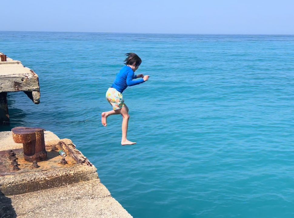 boy jumping from the pier into the blue ocean water at Buneci Beach Albanian Riviera