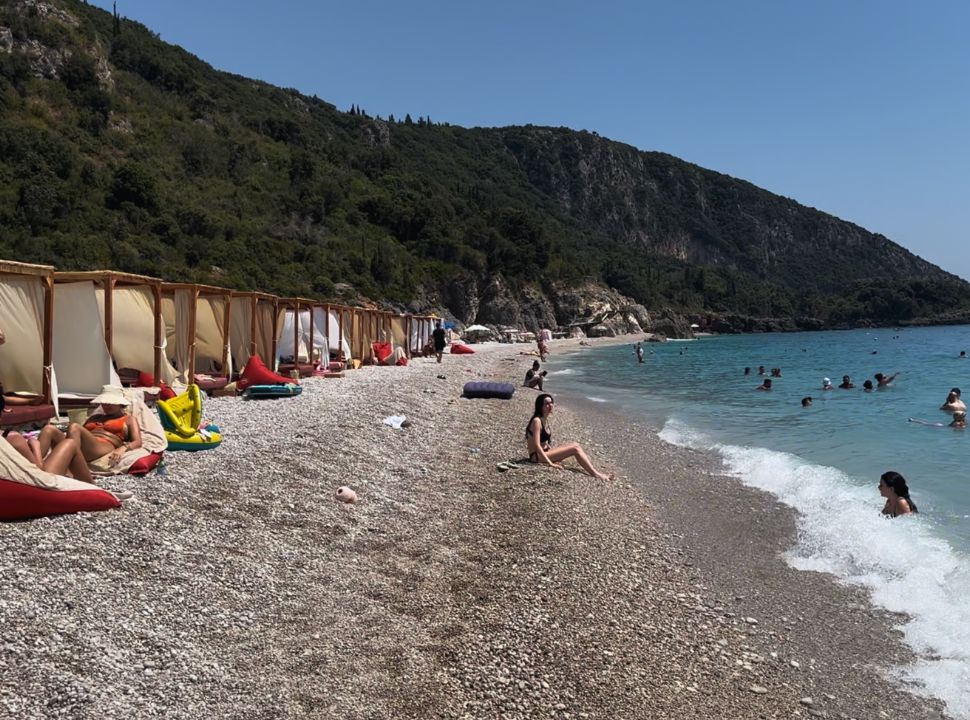 sun gazebos lined along the beach water fron with people swimming and lazing on the beach at Dhermi beach Albania