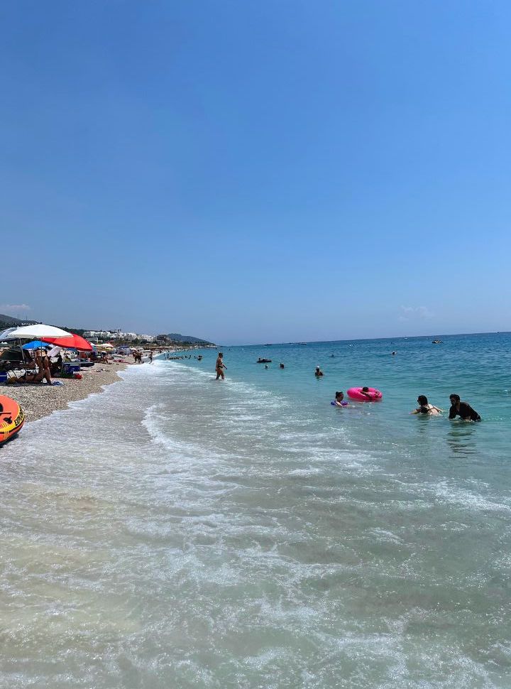 people swimming in the stunning blue ocean, with a row of umbrellas set along the waterfront at Drymades beach Albania