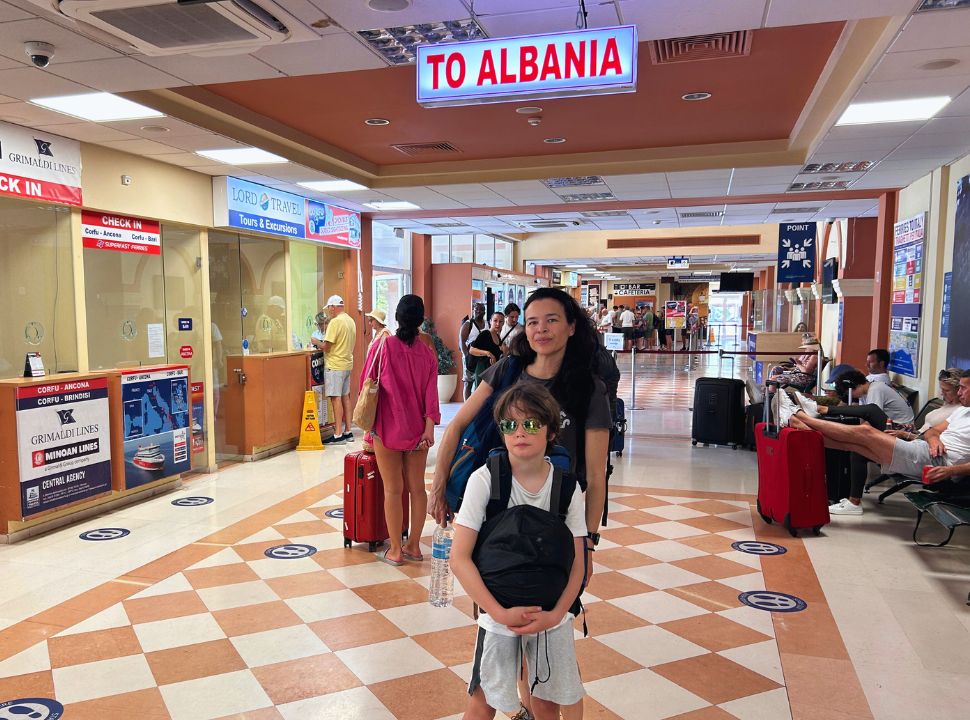 mother and son standing under the sign 'to Albania' at the Corfu Port Terminal