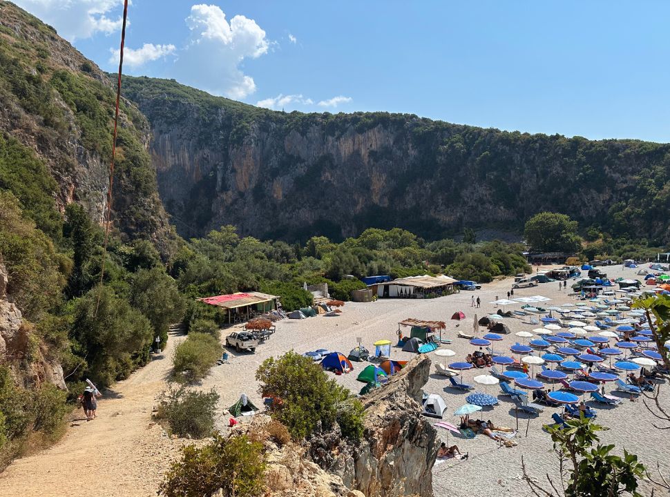 Beach set at the end of an impressive canyon, with trees on the edgjes. Beach is covered with sun umbrellas at the Albanian Riviera