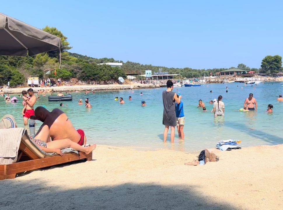 mother helping her son with his swimming goggles at the busy Paradise beach with crystal clear water at Ksamil Albania