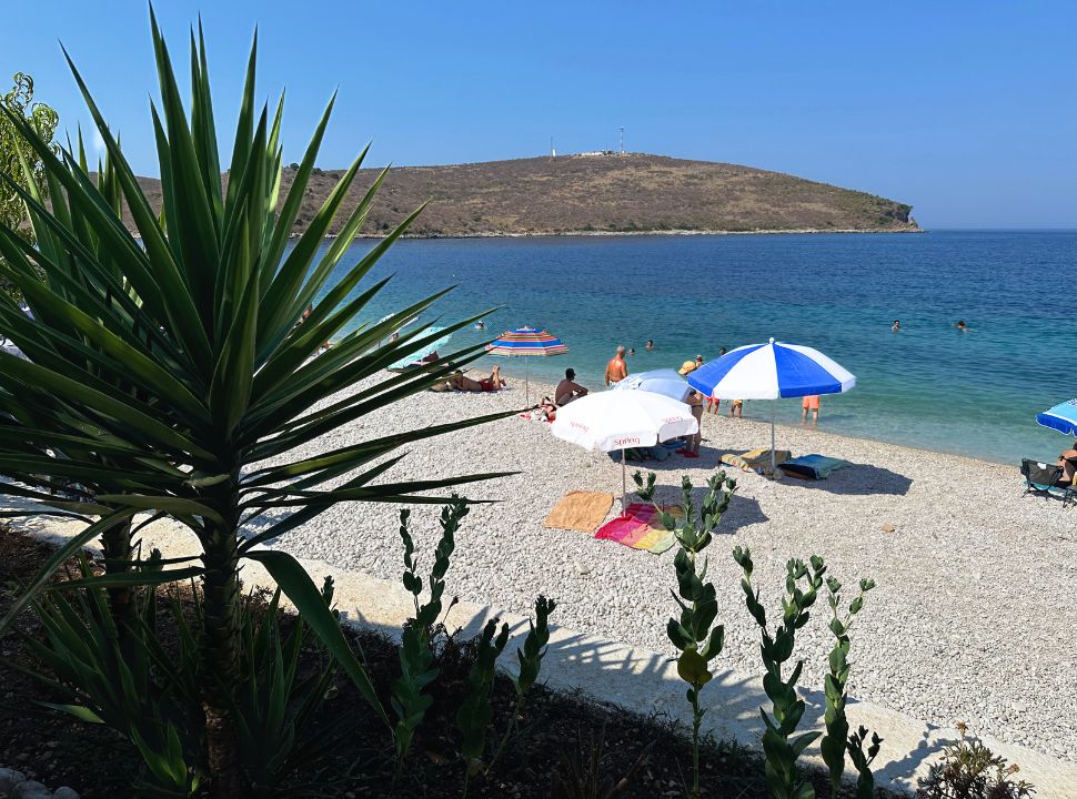 view of Porto Palermo beach Albania from the beach restaurant, sun umbrellas are placed in the sand and people are swimming