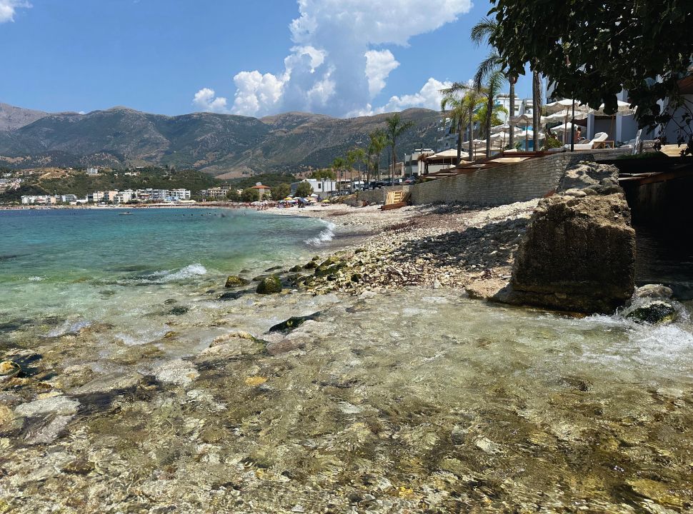 view of Potami beach, with the fresh water running straight into the ocean, accommodation at the beach and in the distance more hotels and sun loungers