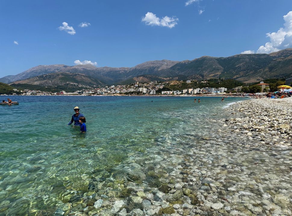 father and son swimming in the clear ocean with in the far distance hotels and mountain range in Himare Albania